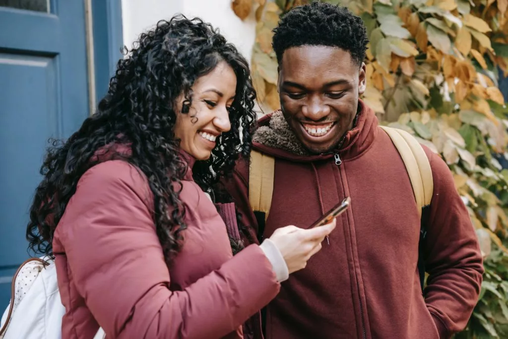 man and woman smiling and looking at their phone