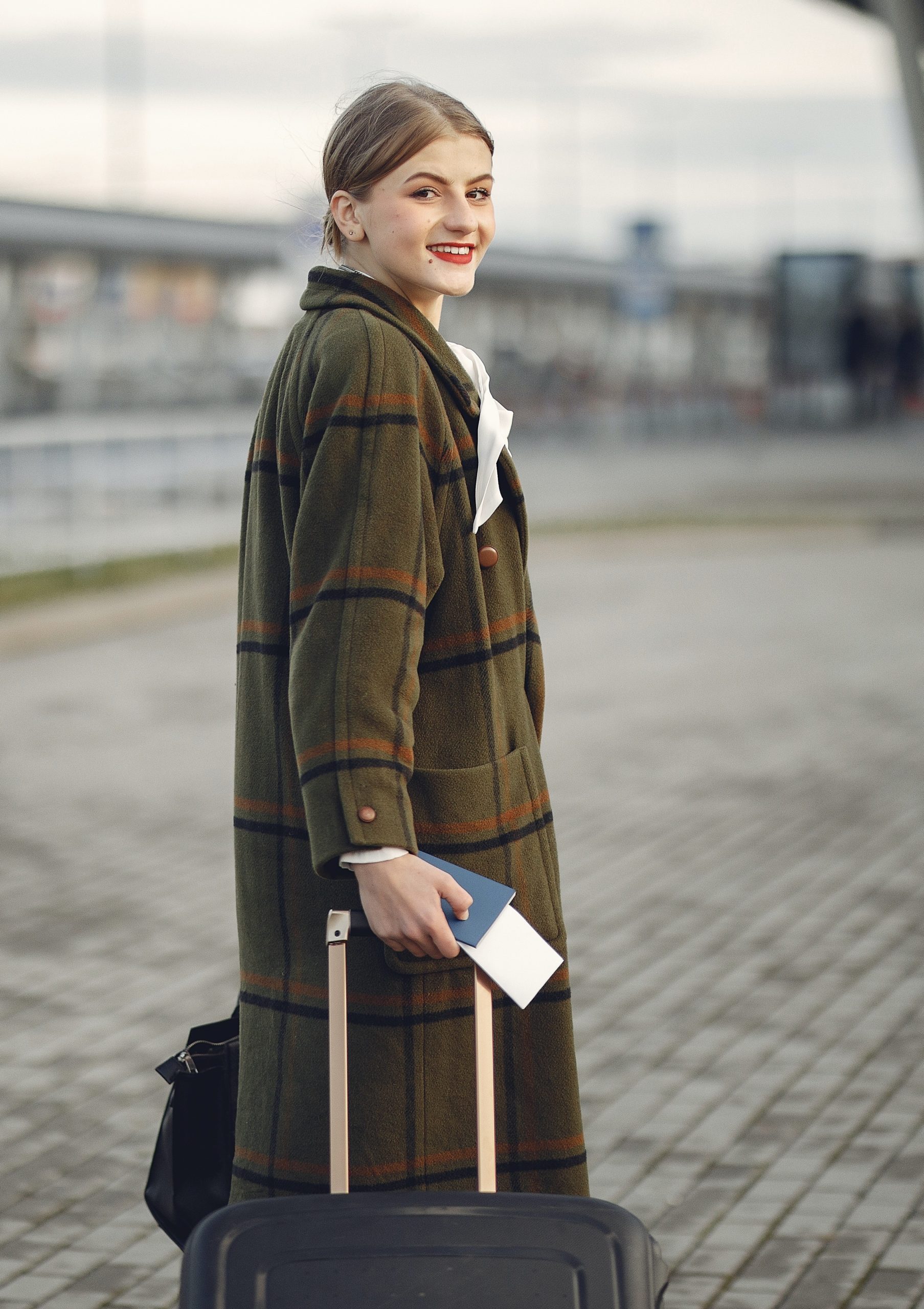 woman in a coat holding her passport, boarding pass and luggage